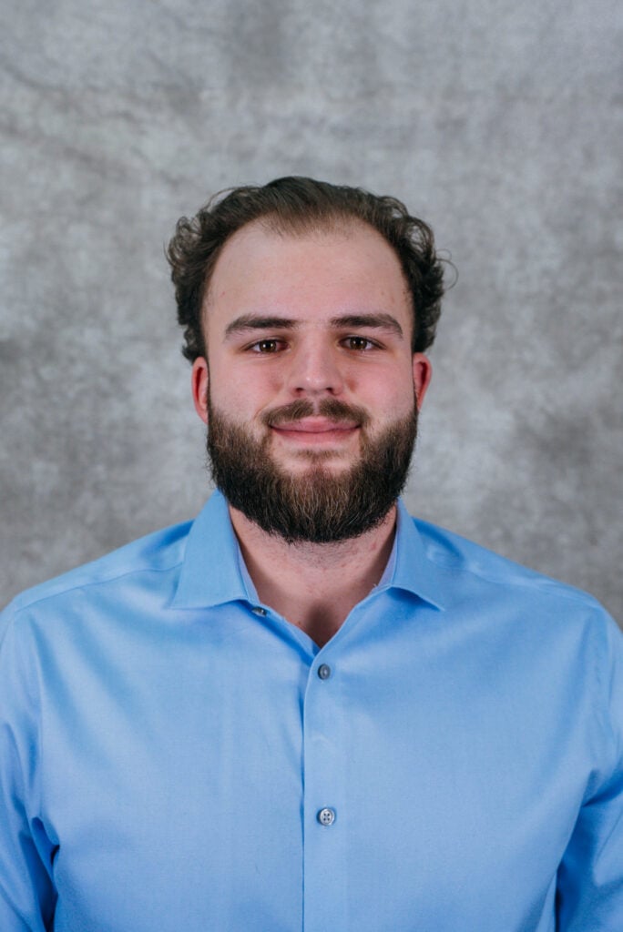A man with a beard wearing a blue shirt. He is smiling and looking at the camera.
