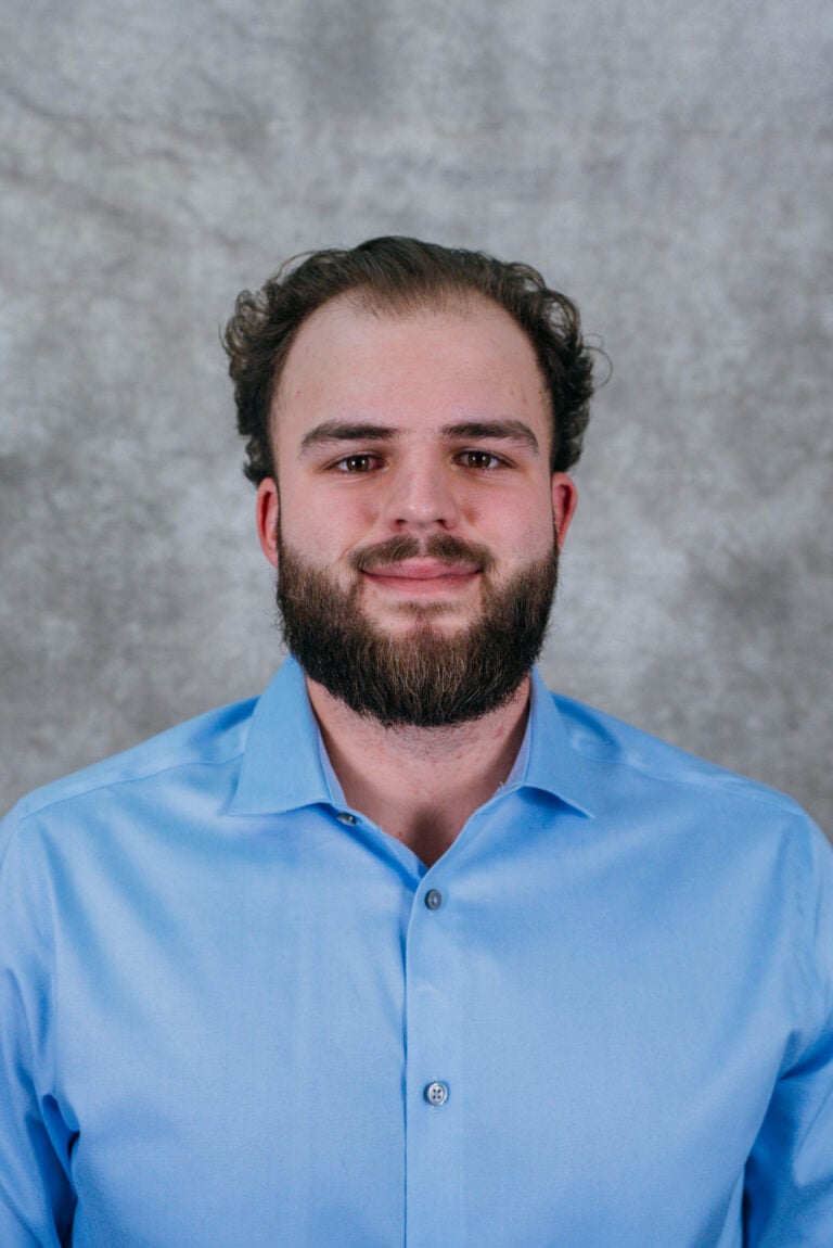 A man with a beard wearing a blue shirt. He is smiling and looking at the camera.