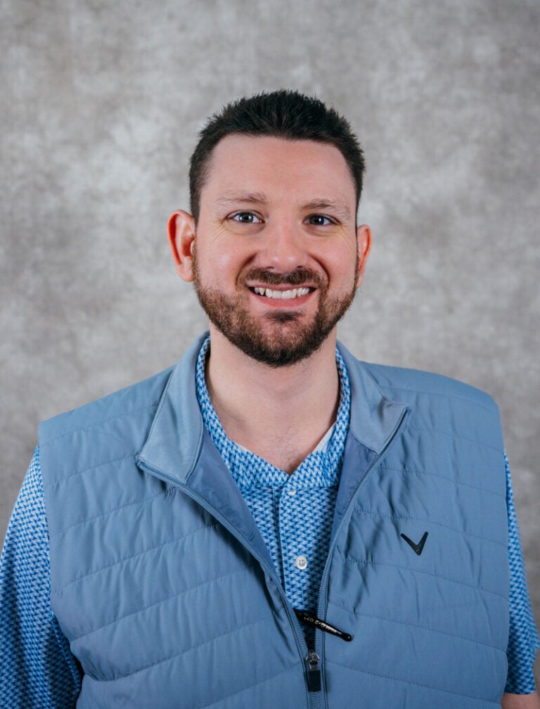 Portrait of a smiling man with short hair and a beard. He is wearing a blue vest.