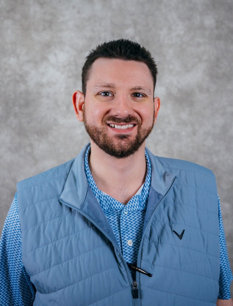 Portrait of a smiling man with short hair and a beard. He is wearing a blue vest.