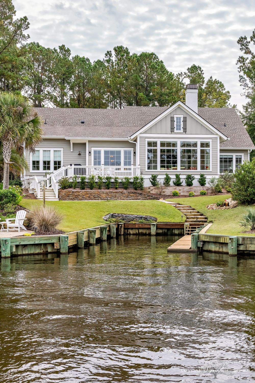 A large house with a dock and palm trees. The house has a gray roof and white trim.