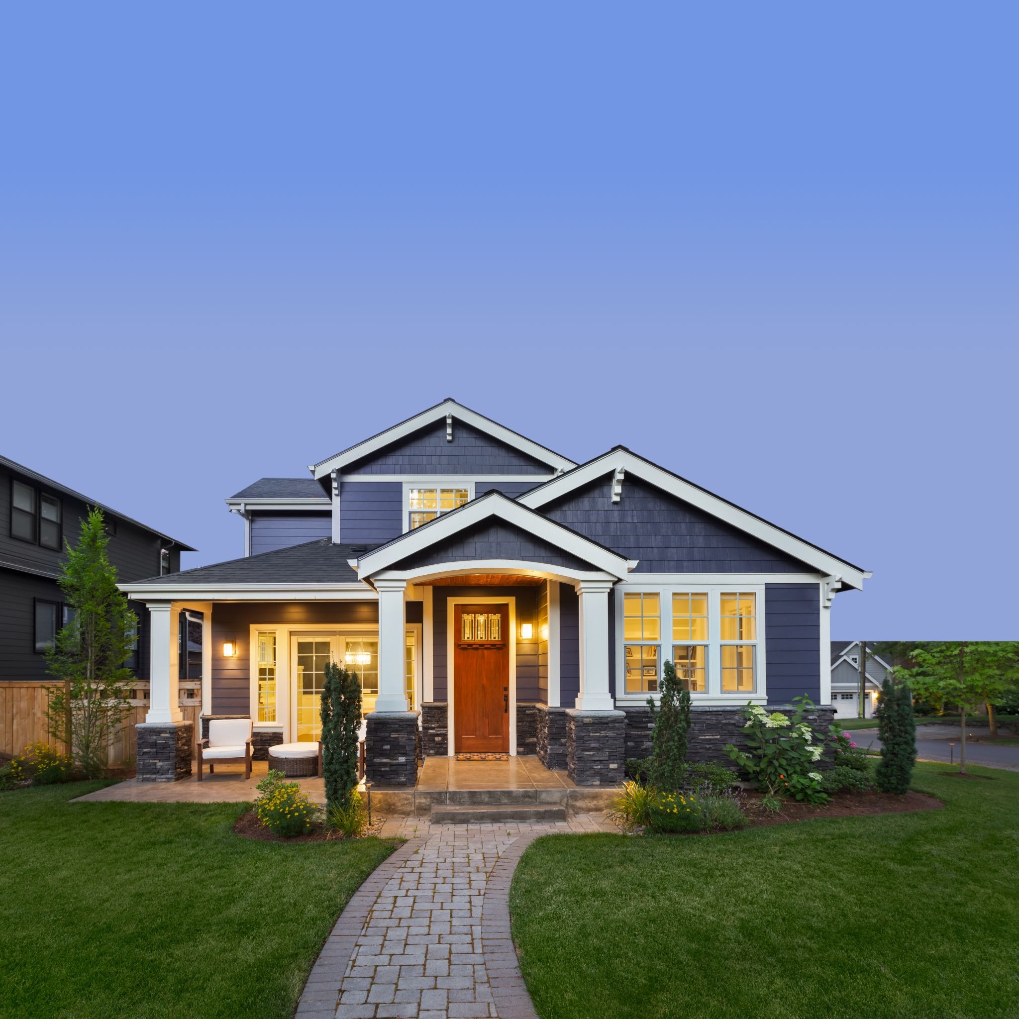 A stunning house with a lit porch and green lawn. The house features a modern design with a warm and inviting exterior.
