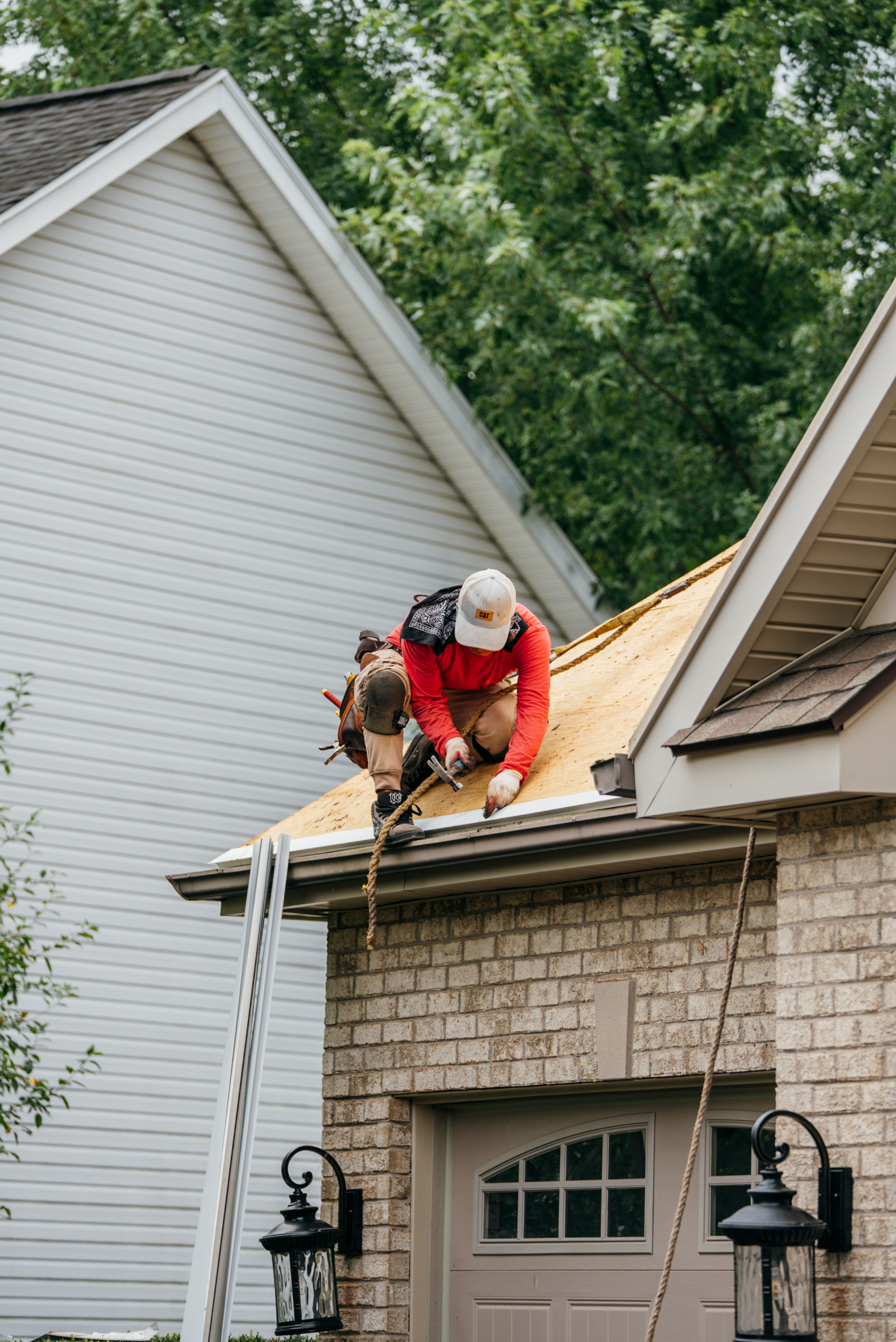 A roofer working on a house roof. The worker is wearing protective gear.