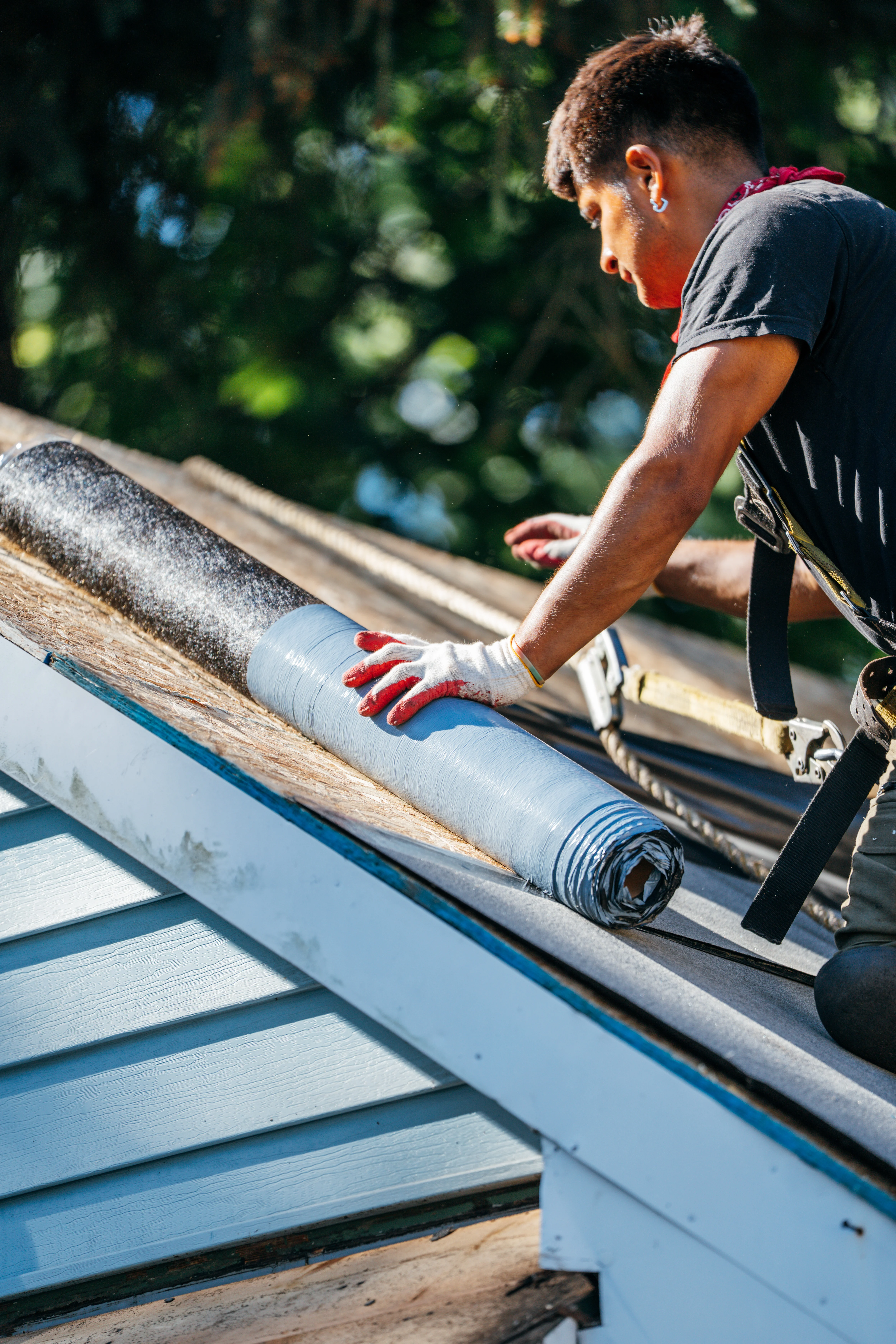 Man in gloves and safety gear applying roofing material
