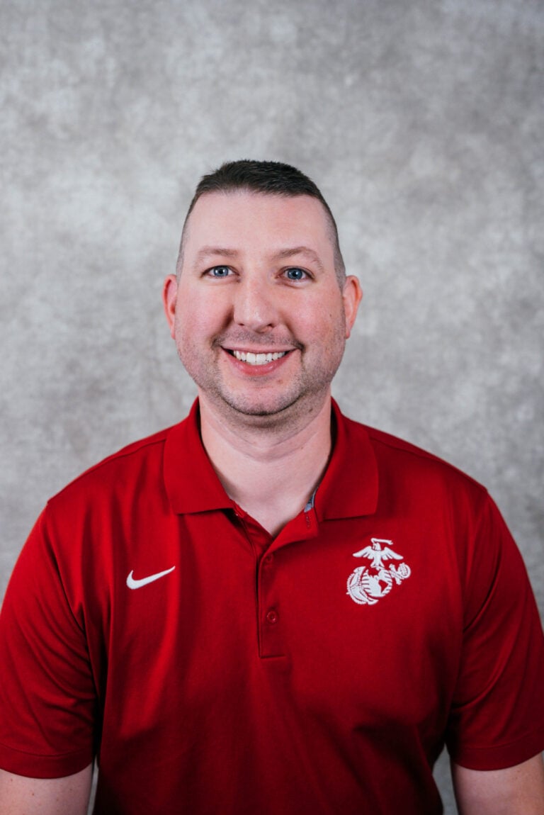 A man wearing a red polo shirt with a white Nike swoosh and Washington State University logo smiles at the camera.