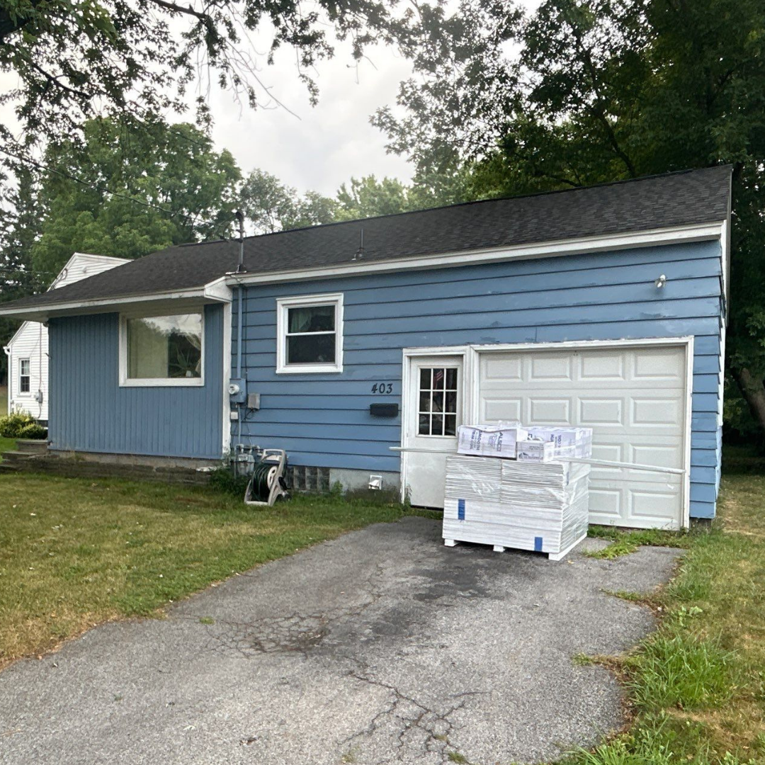 A blue modular home with a white garage door and a pallet of supplies in front.