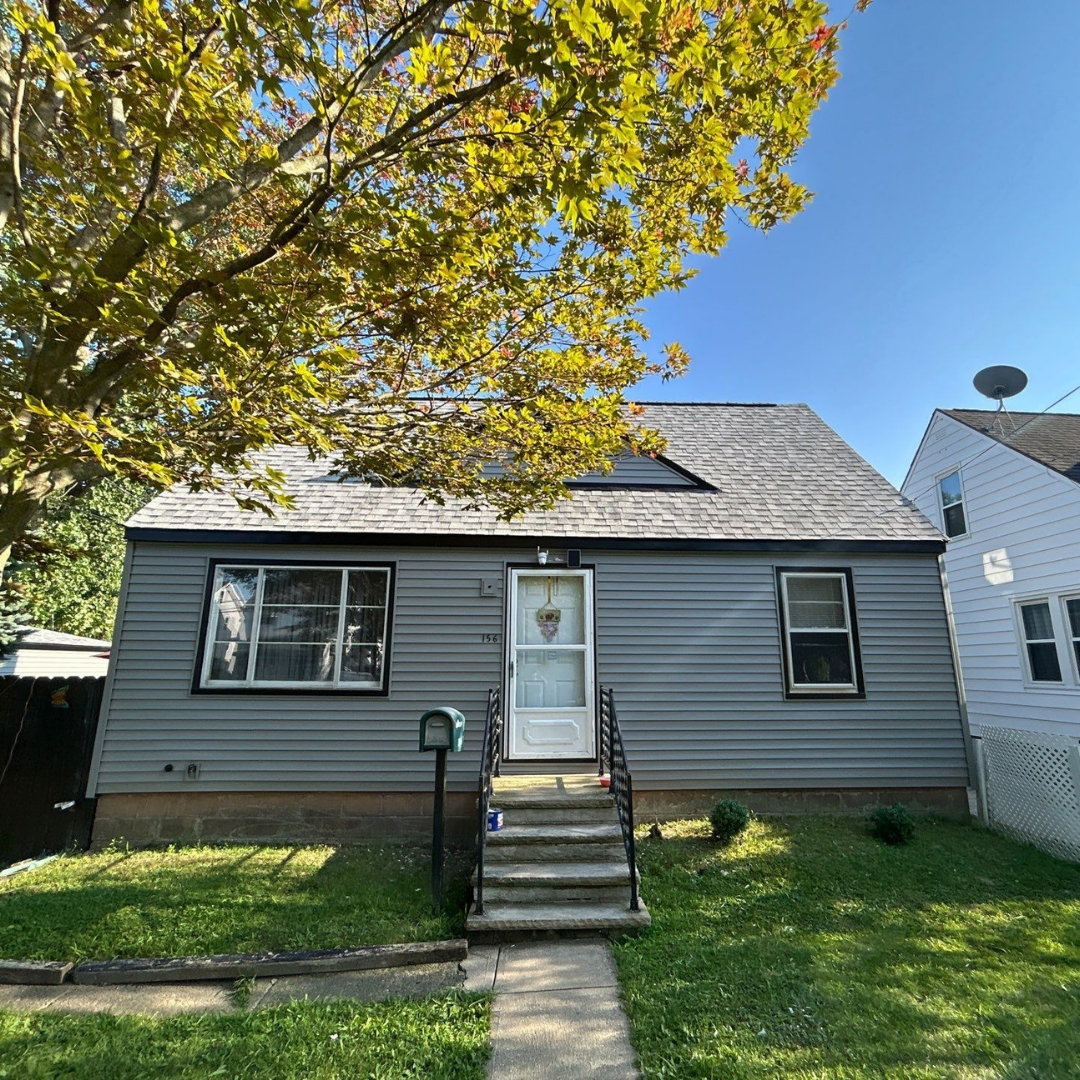 A gray house with a white door and windows, surrounded by a well-maintained green lawn and bordered by trees.