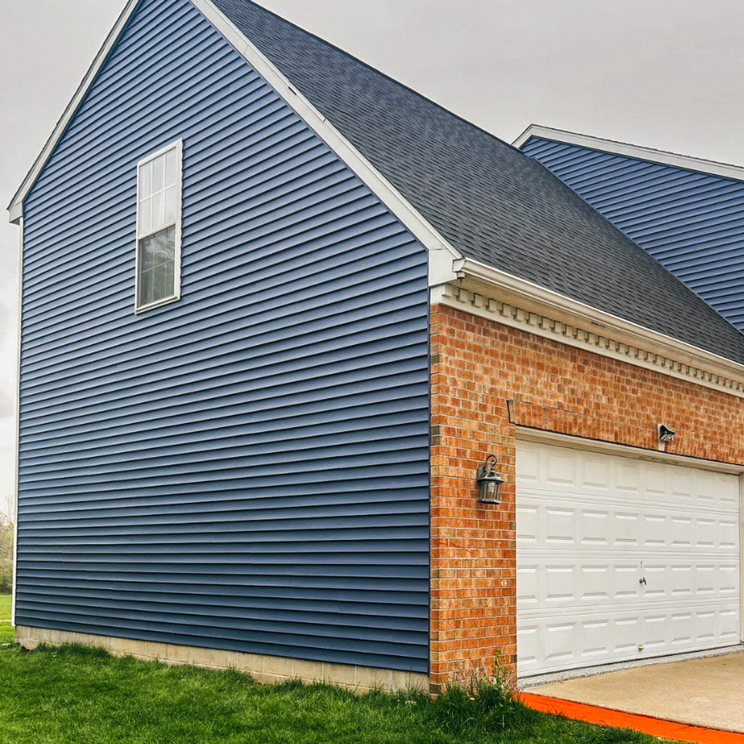 A modern home featuring blue siding, a brick garage area, and a white garage door.