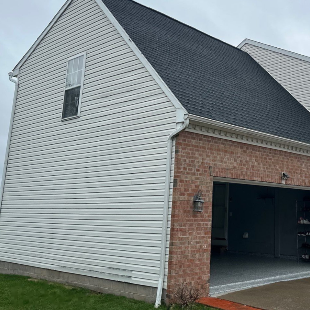 A house with white siding and a brick facade featuring a black shingled roof and garage entrance.