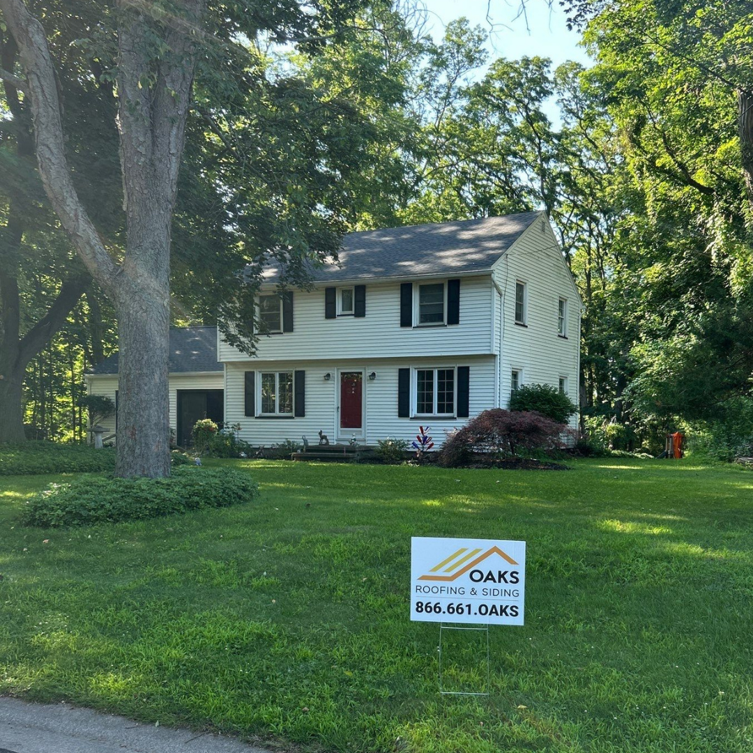 A sign for Oaks Roofing & Siding in front of a residential home with lush greenery.