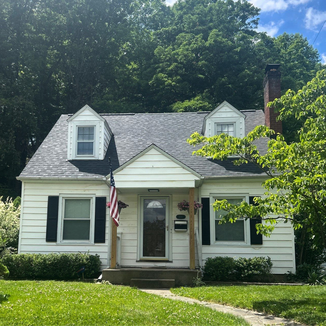 A quaint white cottage features a neatly trimmed lawn and an American flag prominently displayed near the entrance.