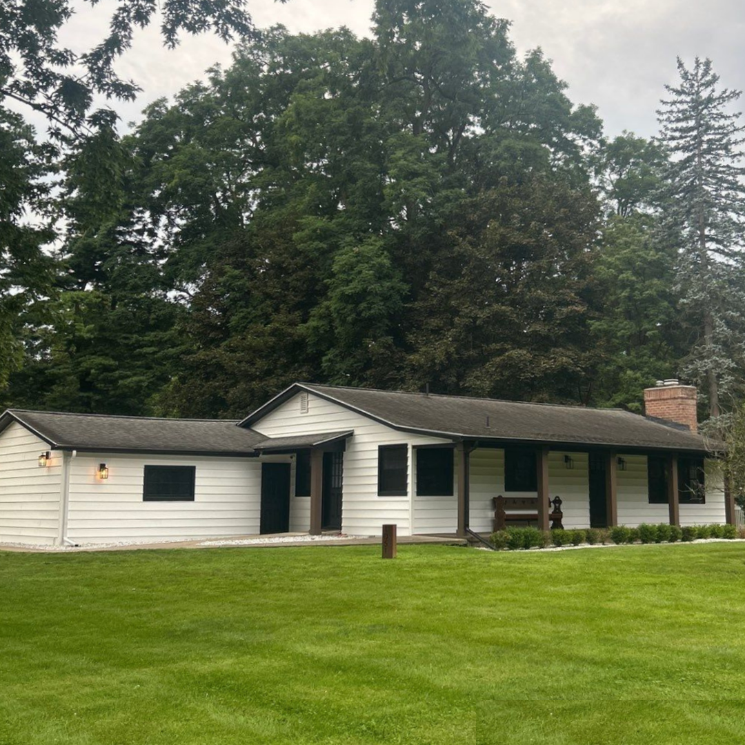 White ranch-style house on lot with large windows and green trees. Spacious front porch with wooden accents.