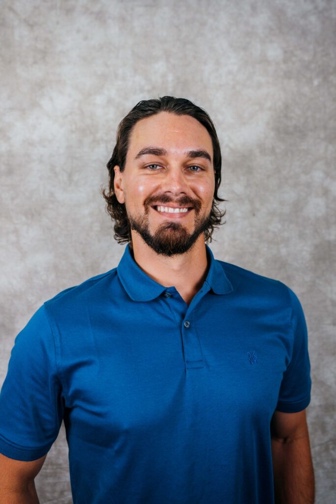 A smiling man with dark hair and a beard wearing a blue polo shirt. Professional headshot against a neutral background.