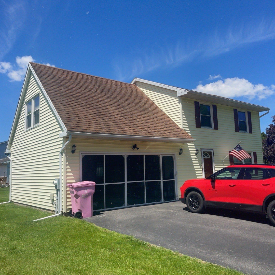 A yellow house featuring a brown shingled roof, green trim, and a red SUV parked in the driveway.