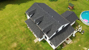 Aerial view of a large white house with a dark shingled roof, surrounded by green lawn and a backyard swimming pool.