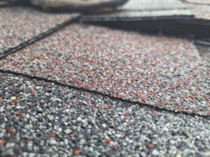 Close-up view of textured asphalt shingles in multi-color red, gray, and black tones overlapping on a roof surface.
