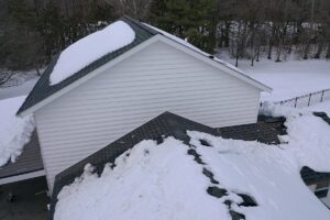 Aerial view of a white garage with dark shingles and snow accumulation on the roof.