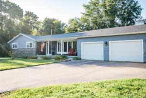 A comfortable single-story house with a gray exterior and a two-car garage, featuring a red rocking chair on the porch and a well-maintained lawn.