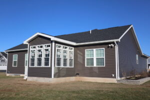 A modern single-story house with brown siding, white trim, and a dark roof under a clear blue sky, shown in multiple angles.