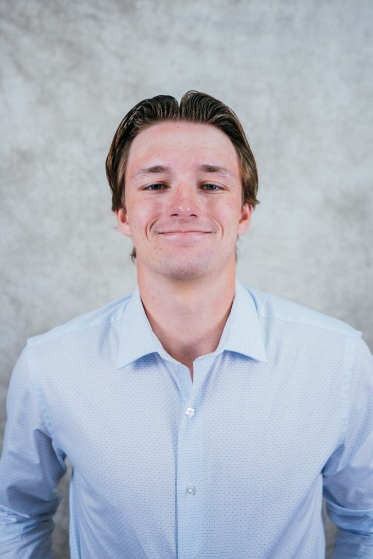 A smiling man in a light blue dress shirt against a neutral background. Professional corporate headshot for website profile.