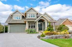A light blue two-story suburban home under a blue sky. The image includes views of the roof, garage, and front yard landscaping.