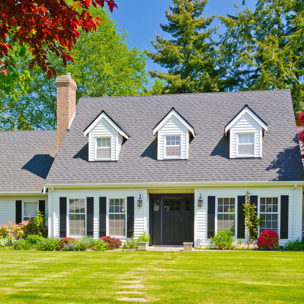 White house with gray roof and green lawn. The house has a well-manicured lawn and trees in the background.