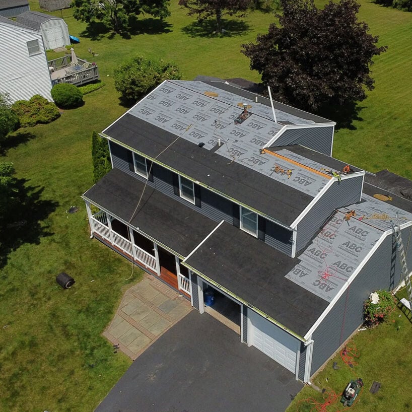 Aerial view of house with roof under construction A house with a partially removed roof. Workers are on the property.