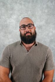 Man with beard and glasses looking forward. He is wearing a striped shirt.