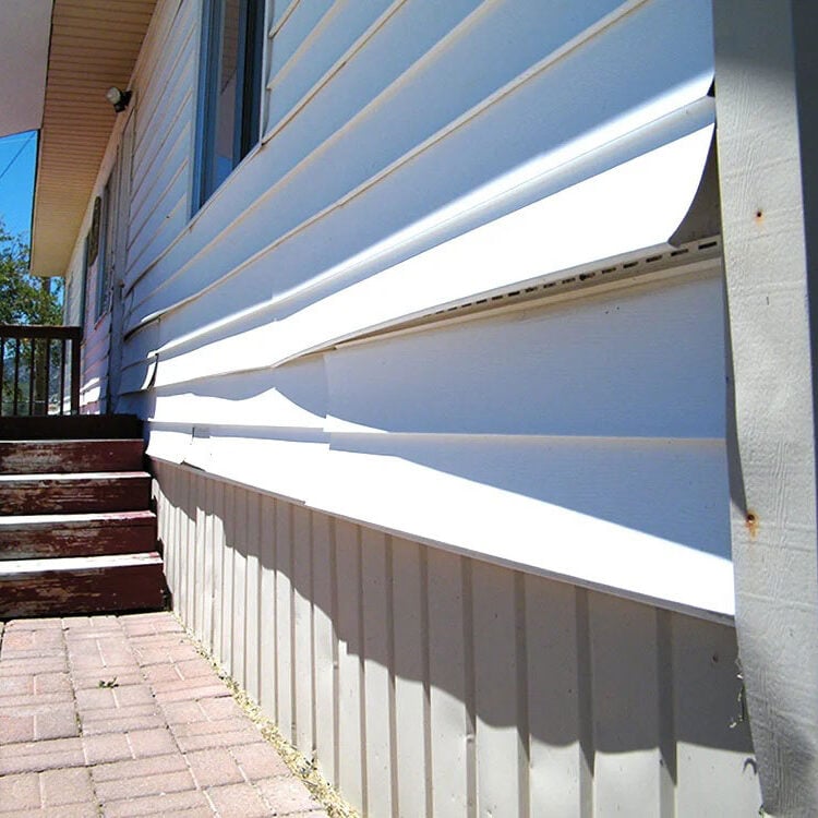 Damaged white vinyl siding on a house. A brick pathway and wooden steps are visible.