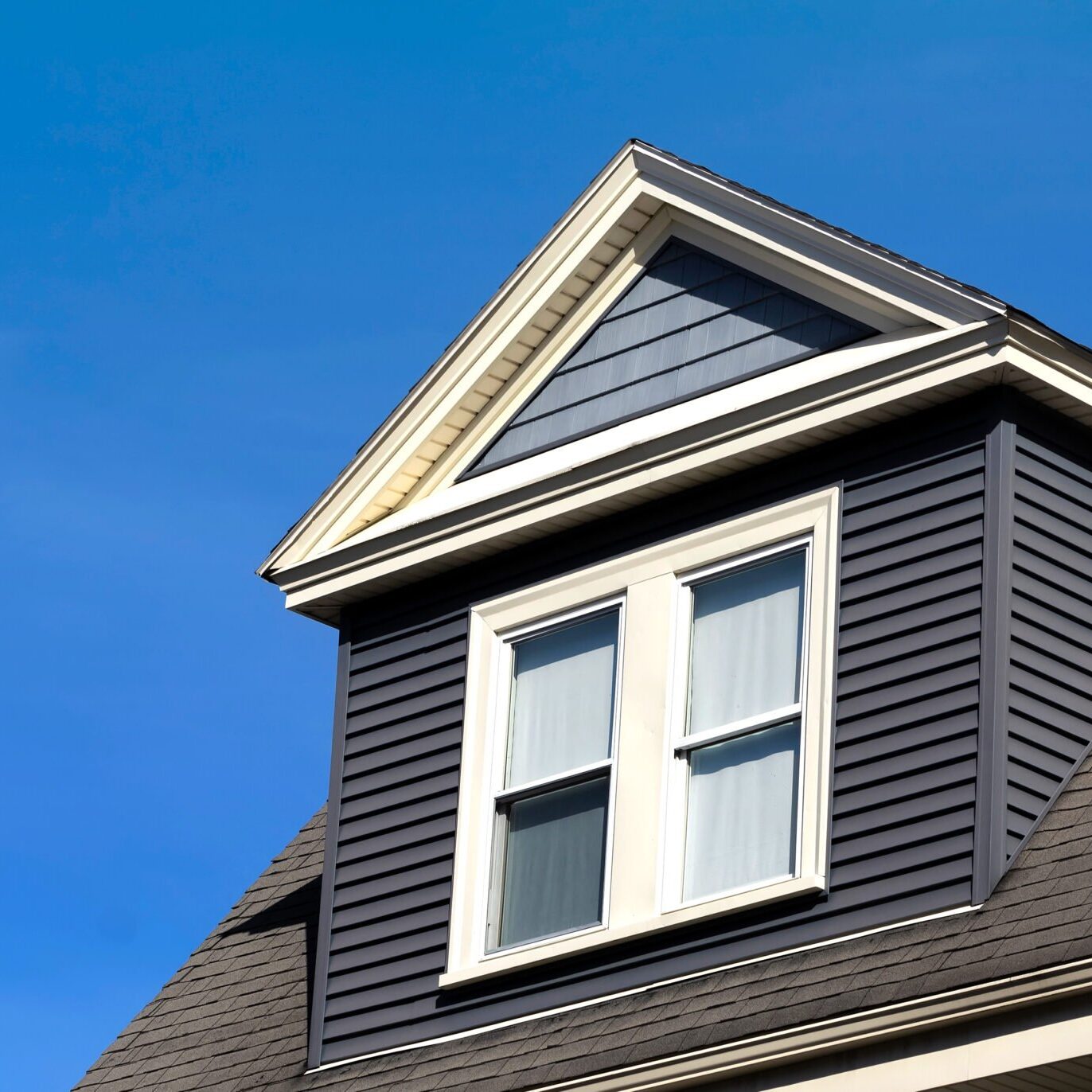 A dormer window on a dark blue house with white trim