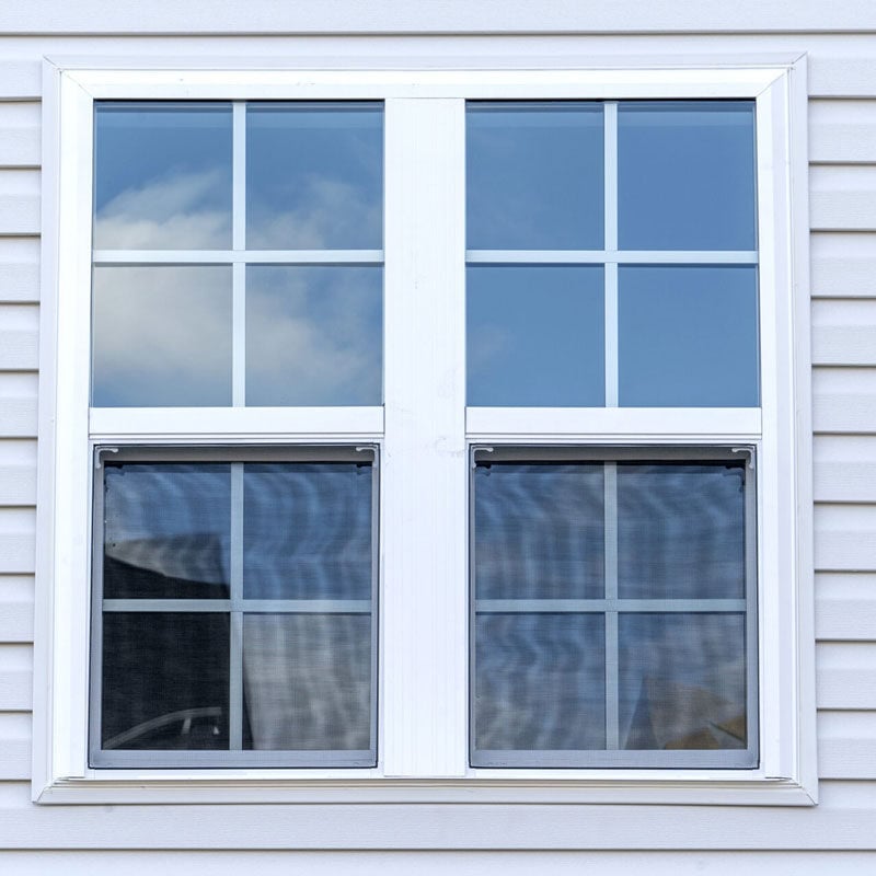 White Double Hung Window with Reflection A white double hung window reflecting blue sky and clouds. The window is set in a gray siding wall.