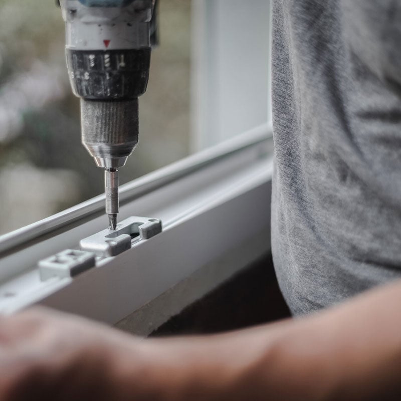 Person drilling into a window frame A person using a drill on a window. The person is wearing a gray t-shirt.