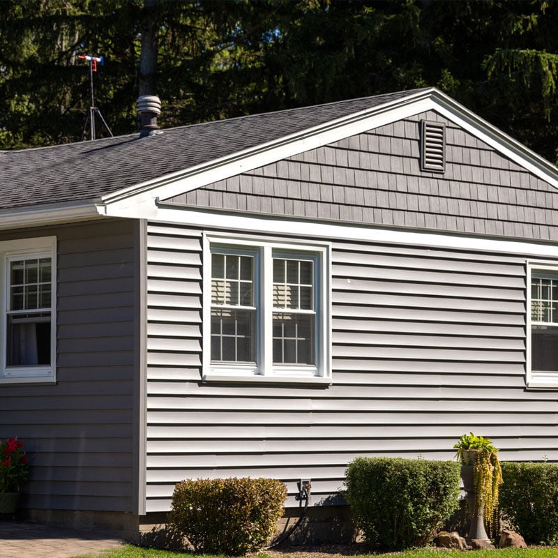 Gray house with white trim and bushes Gray house exterior with white trim and windows. A small garden with bushes in front.