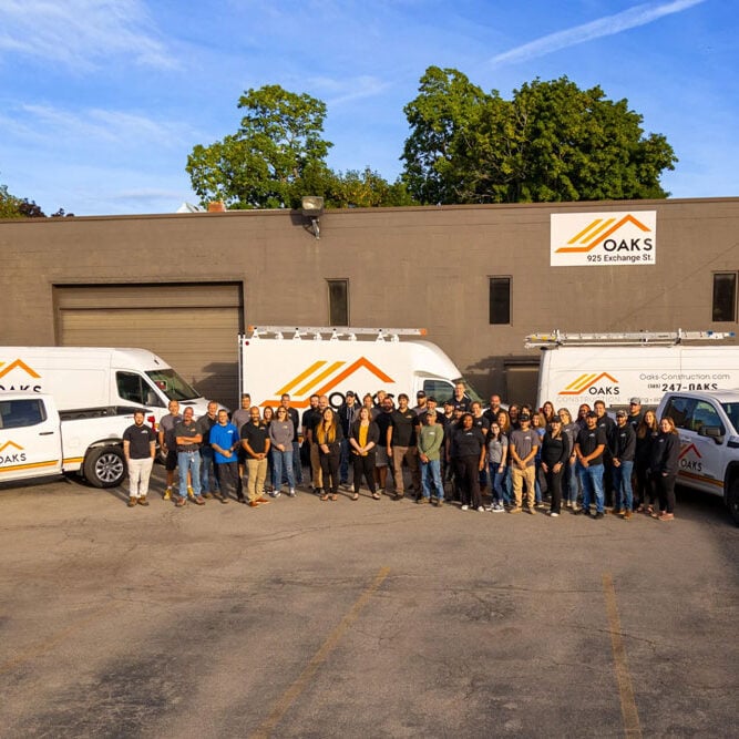 A group of people standing together outside. Several white vans.