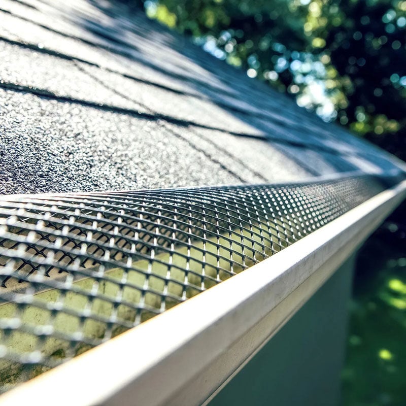 A gutter guard installed on a sloping roof to prevent debris. The guard is made of metal mesh.