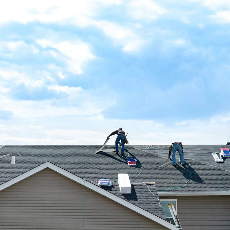 Roofers working on a house with gray shingles Workers installing new roof on a residential house. Roofing professionals at work.