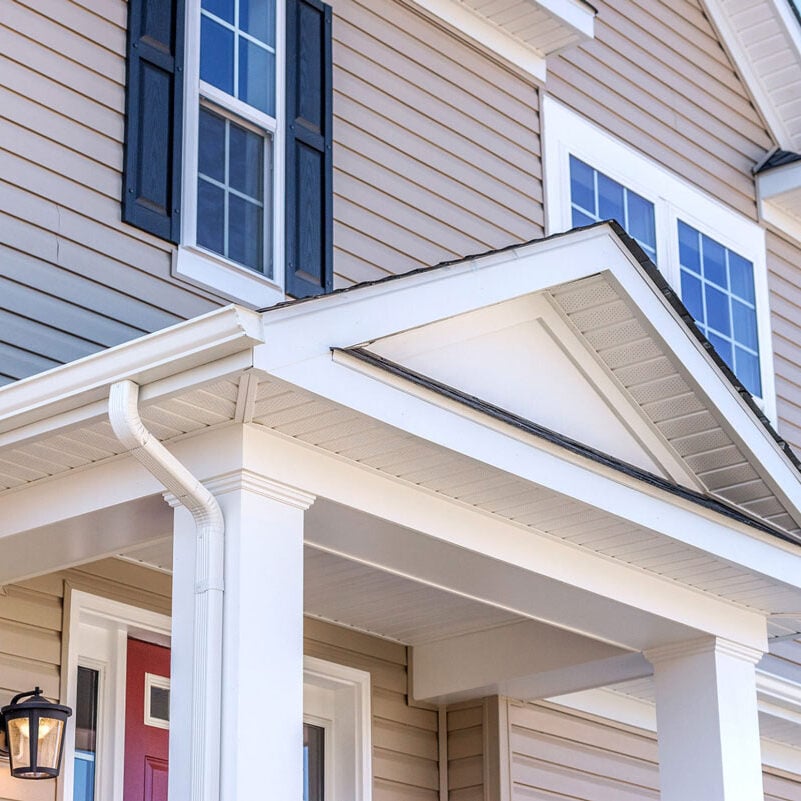 House Exterior with Covered Porch and Gutters A house with a covered porch and white gutters. The exterior features beige siding and black shutters.