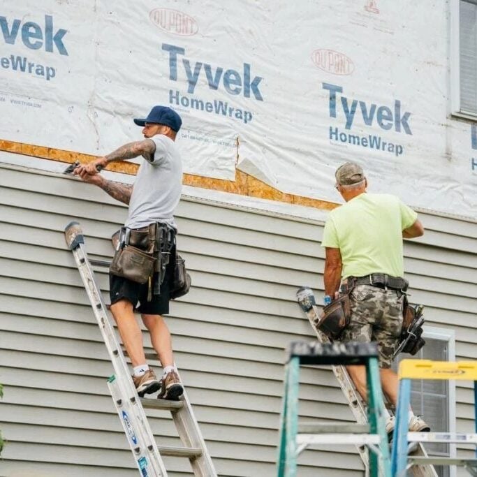 Workers Installing Tyvek HomeWrap on House Exterior Two workers on ladders applying Tyvek HomeWrap to a house