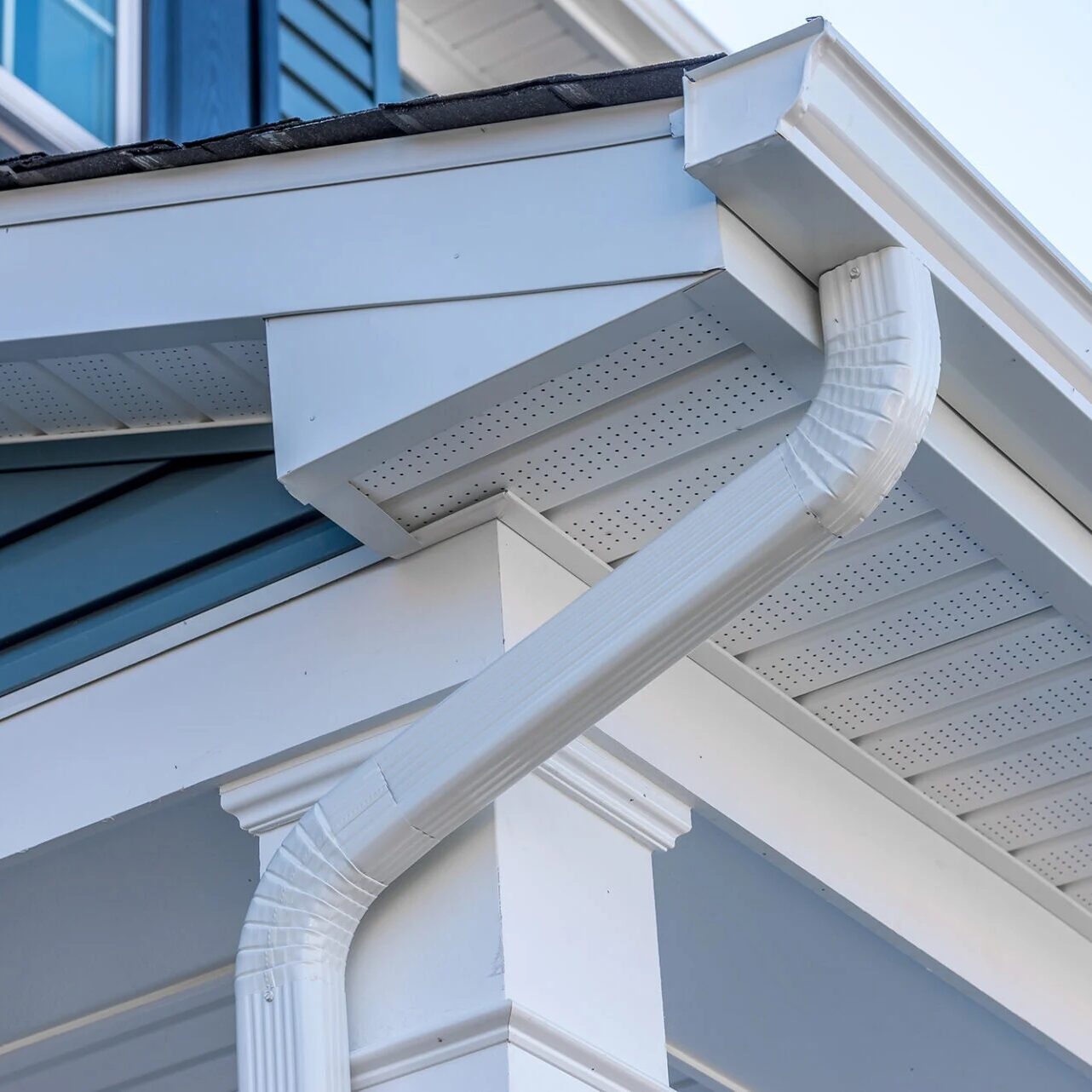A white gutter system on a house with blue siding. The gutter is attached to the eaves.