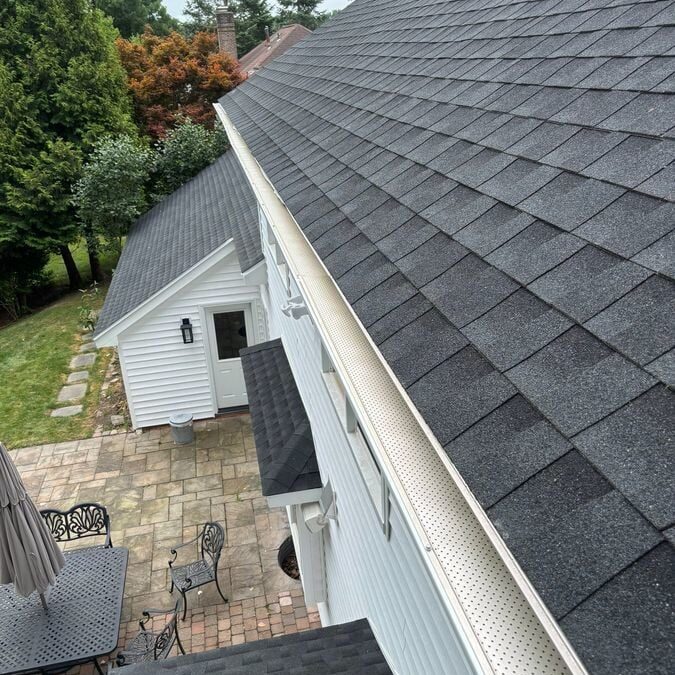 A house with a black roof and white gutters. The house has a patio area with tables and chairs.