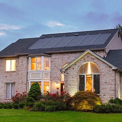 A large house with solar panels on its roof. The house is lit up from within.