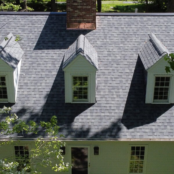 Aerial View of House with Gray Roof A house with a gray roof and white trim. The house has multiple windows and a chimney.