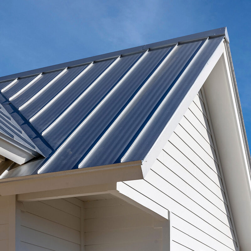 Metal roof on a house with white siding. The roof is made of metal panels.