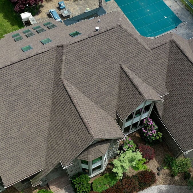 A large house with a brown roof and a swimming pool. The house has a well-manicured garden.