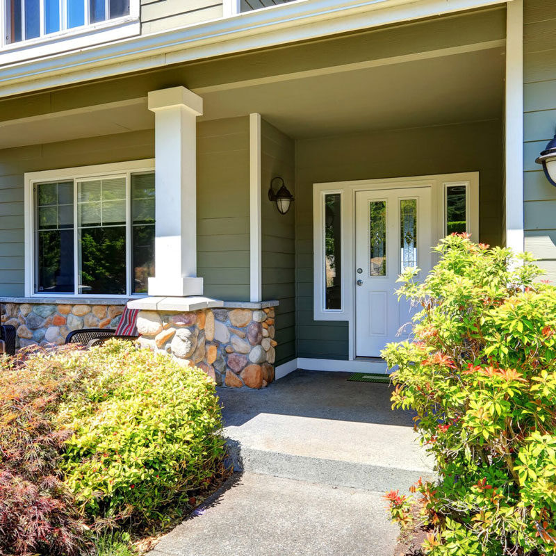 Beautiful House with Covered Porch and Green Bushes A house with a covered porch and green bushes. The house has a white front door.