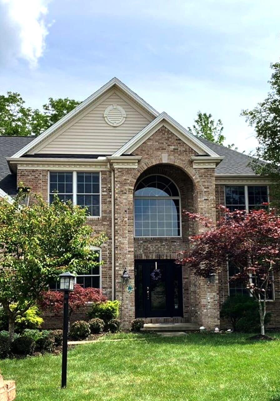 A large house with a brick and siding exterior. The house has a well-manicured lawn and trees.
