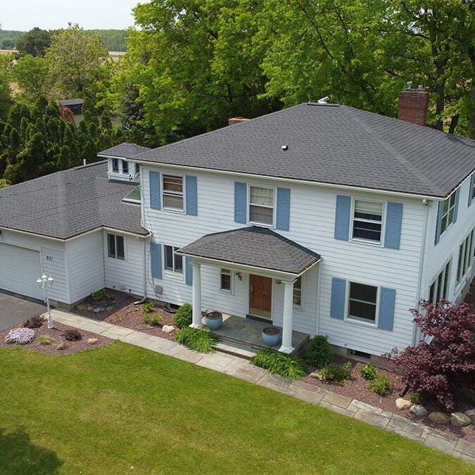 A large white house with blue shutters and a green lawn. The house has a grey roof and a brown front door.