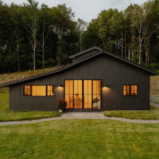 Modern Dark House in Nature A modern dark house with lit windows in a natural setting. The house has a large glass door and windows.