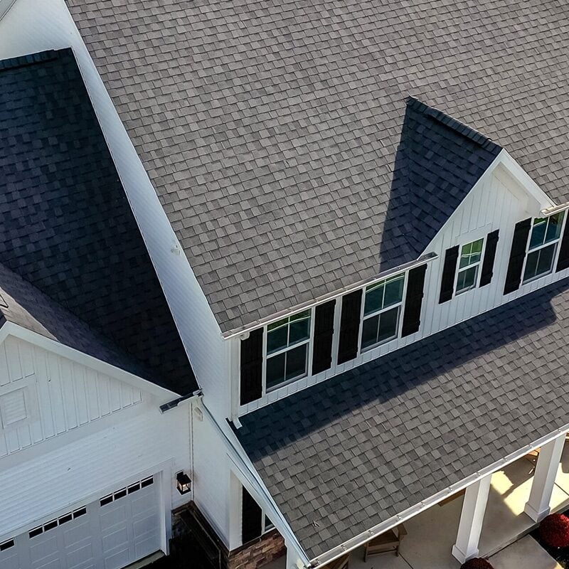 Aerial view of a white house with a grey roof. The house features a garage and black decorative shutters.