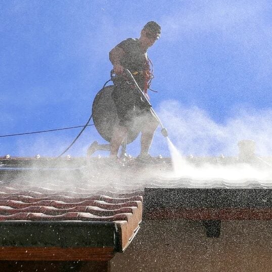 Man Cleaning Roof with Power Washer Man power washing a roof on a sunny day.